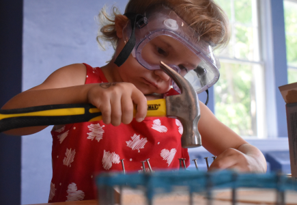 child focusing on hammering nails