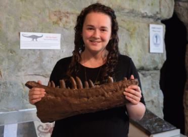 smiling woman holding a dinosaur jawbone replica 