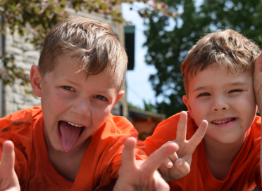 two boys looking at camera with peace signs, one smiles and one sticks out his tongue