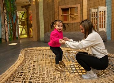 child jumps on treehouse net with caregiver holding hands